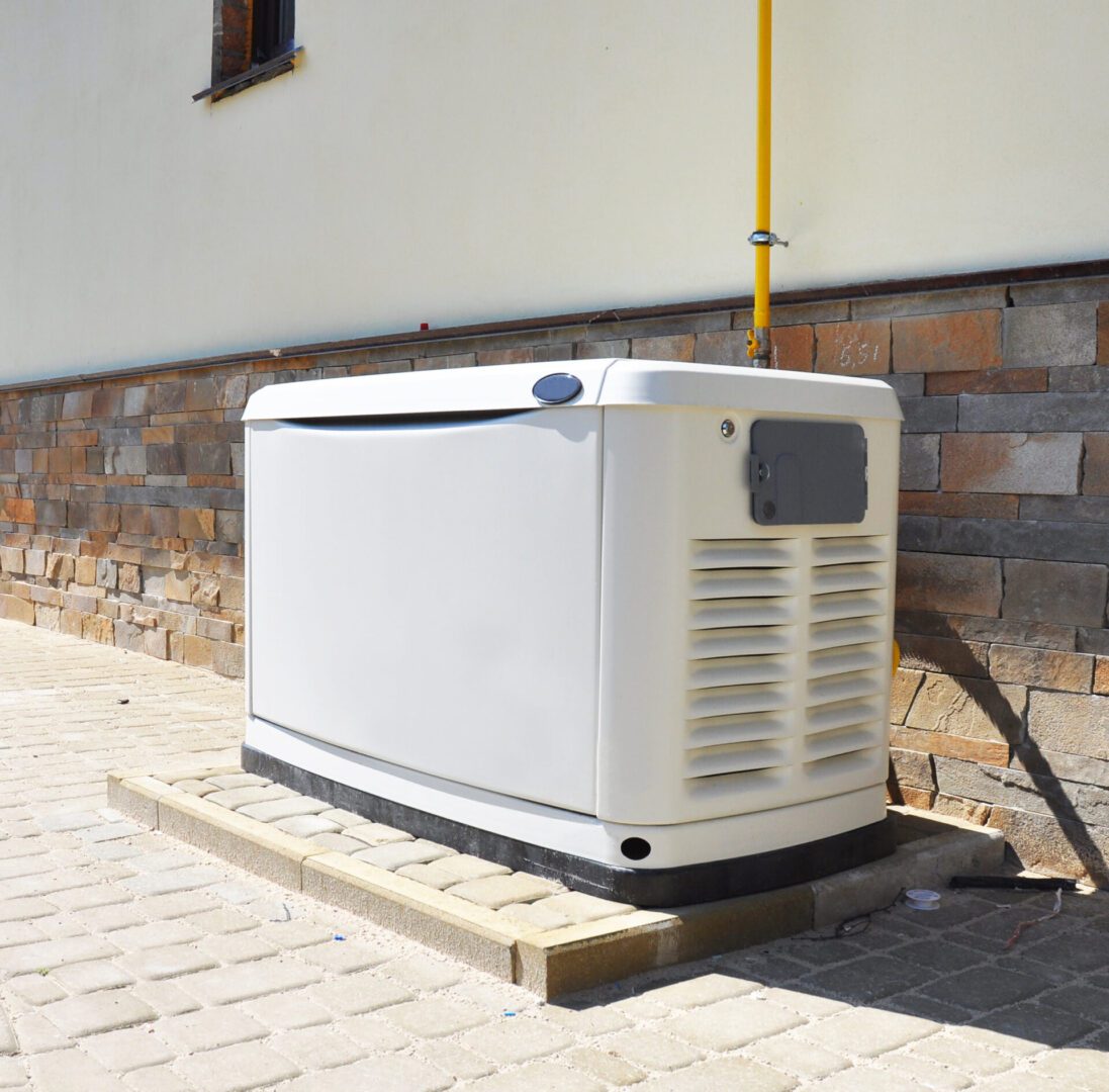 A large, white outdoor generator sits on a concrete base against a brick and stucco wall, connected to a yellow utility pipe.