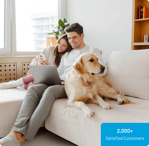 Couple sitting on a couch with a laptop and a dog; sticker reads "2,000+ Satisfied Customers.